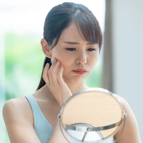 口元を鏡でみて不満そうな顔の女性